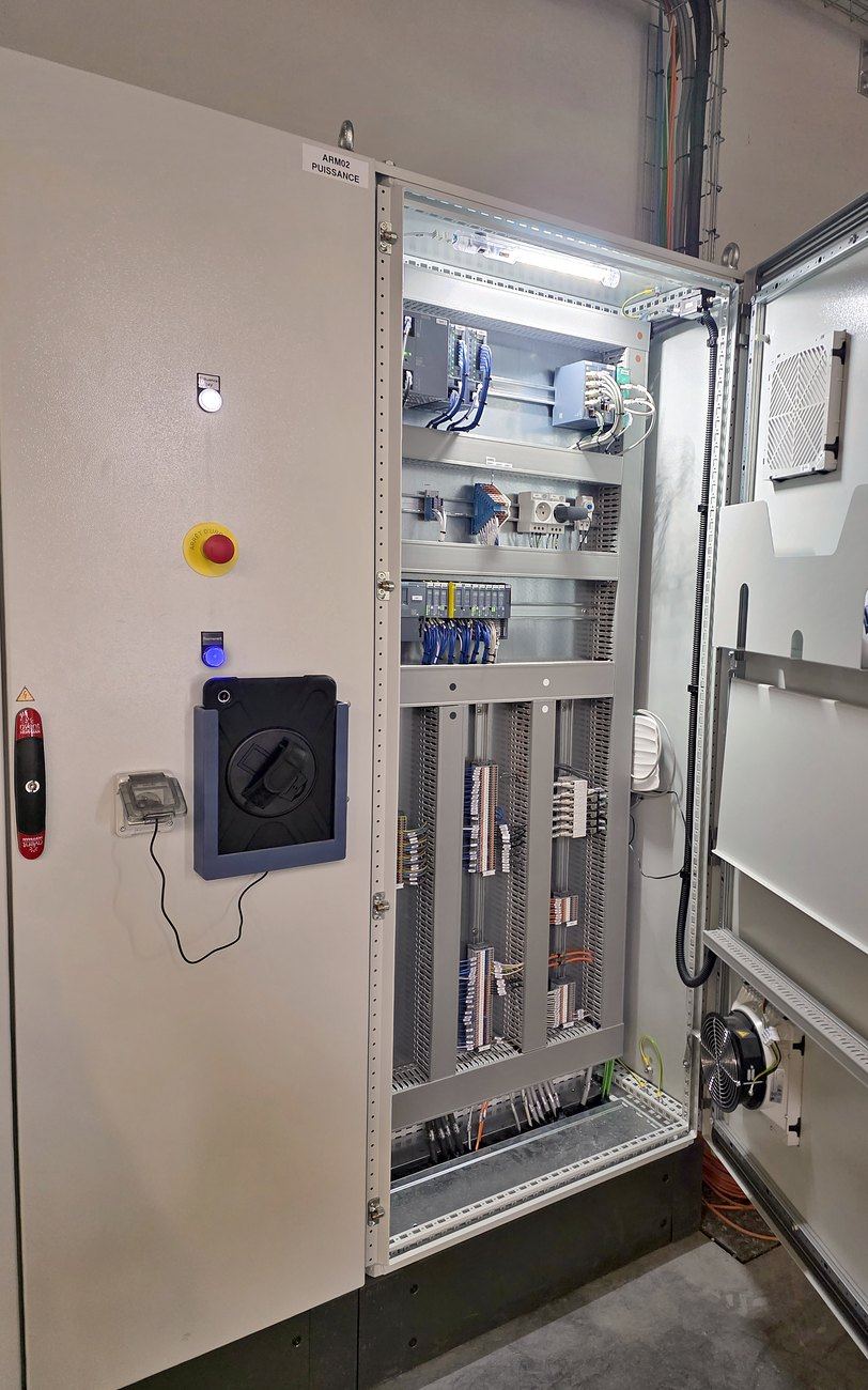L'armoire installée sur le site du client, portes ouvertes, avec une tablette de supervision fixée sur la porte.